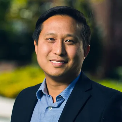 David Wang, PhD, smiling, with short dark hair, wearing a navy blazer over a blue collared shirt, outdoors