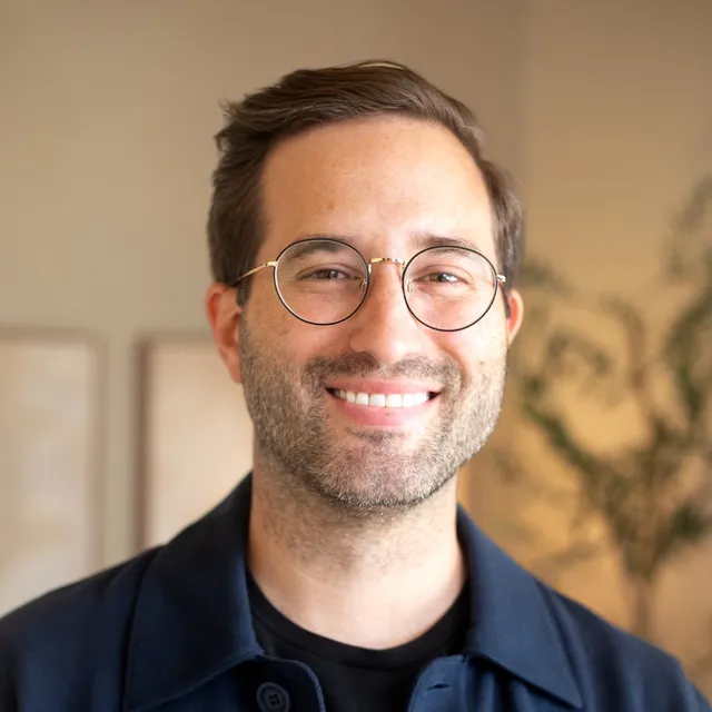 Christopher Schadt, PsyD, smiling, wearing round glasses and a navy shirt