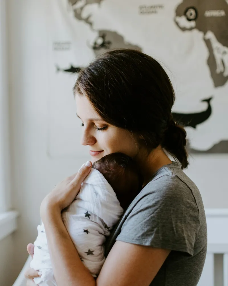 A mother holding her sleeping newborn close, the kind of tender, tiring postpartum season Coastal Therapy Group supports